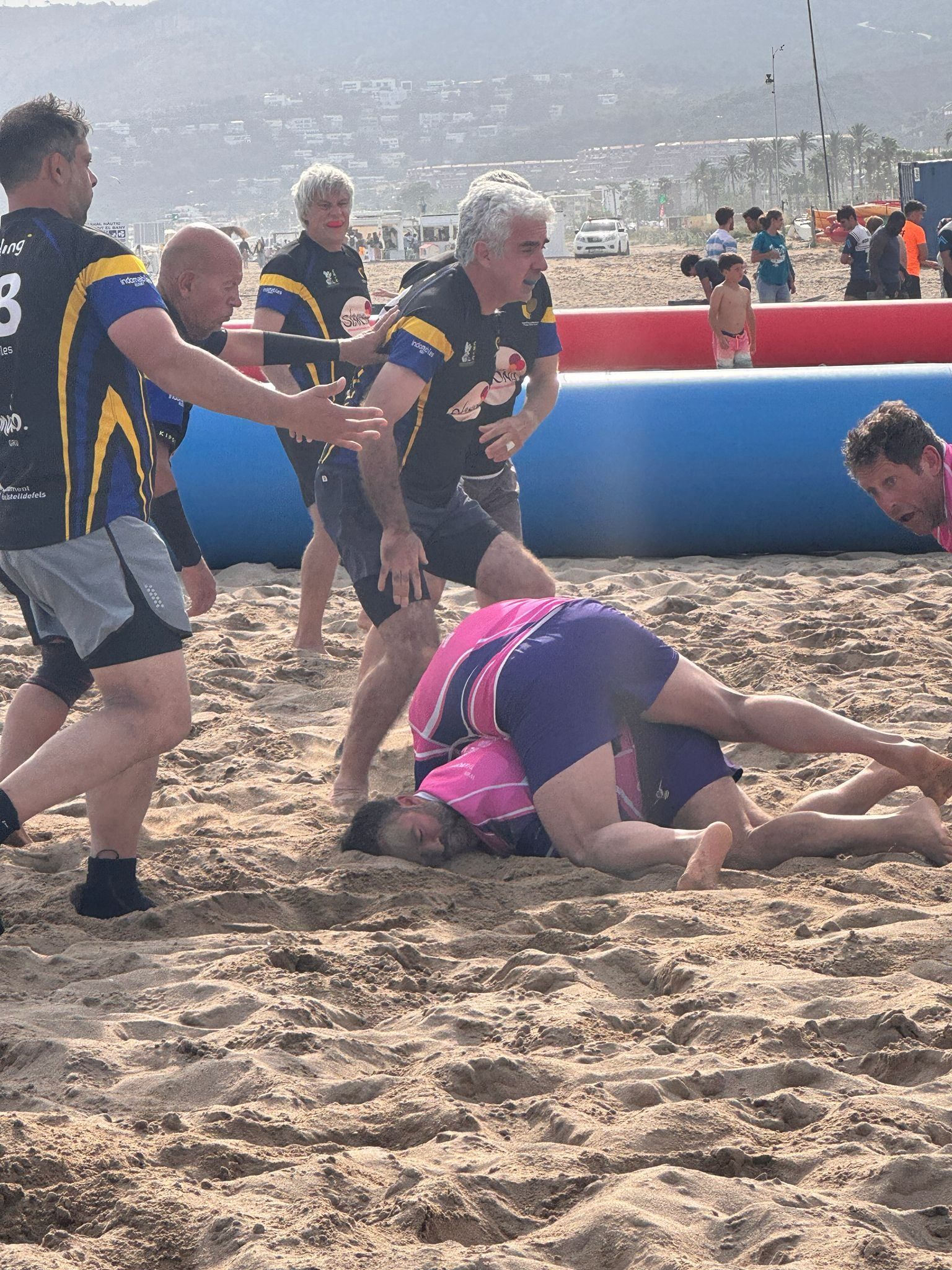 Un jugador dels Flying Rugby Pigs fa un placatge a la sorra mentre els rivals arriben al ruck