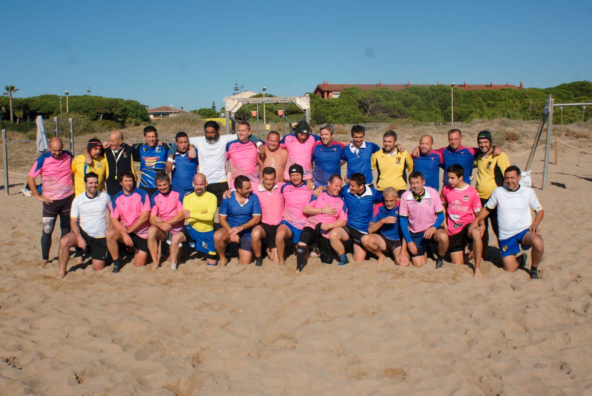 Foto de grup dels Flying Rugby Pigs i amics, amb samarretes de colors, a la sorra de la platja