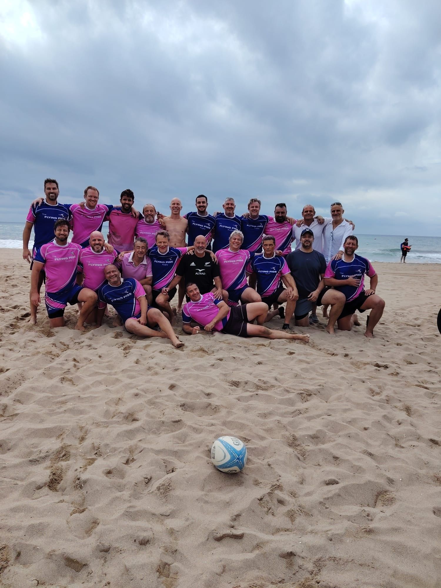 L'equip dels Flying Rugby Pigs, amb samarretes roses i blaves, somrient a la sorra davant del mar