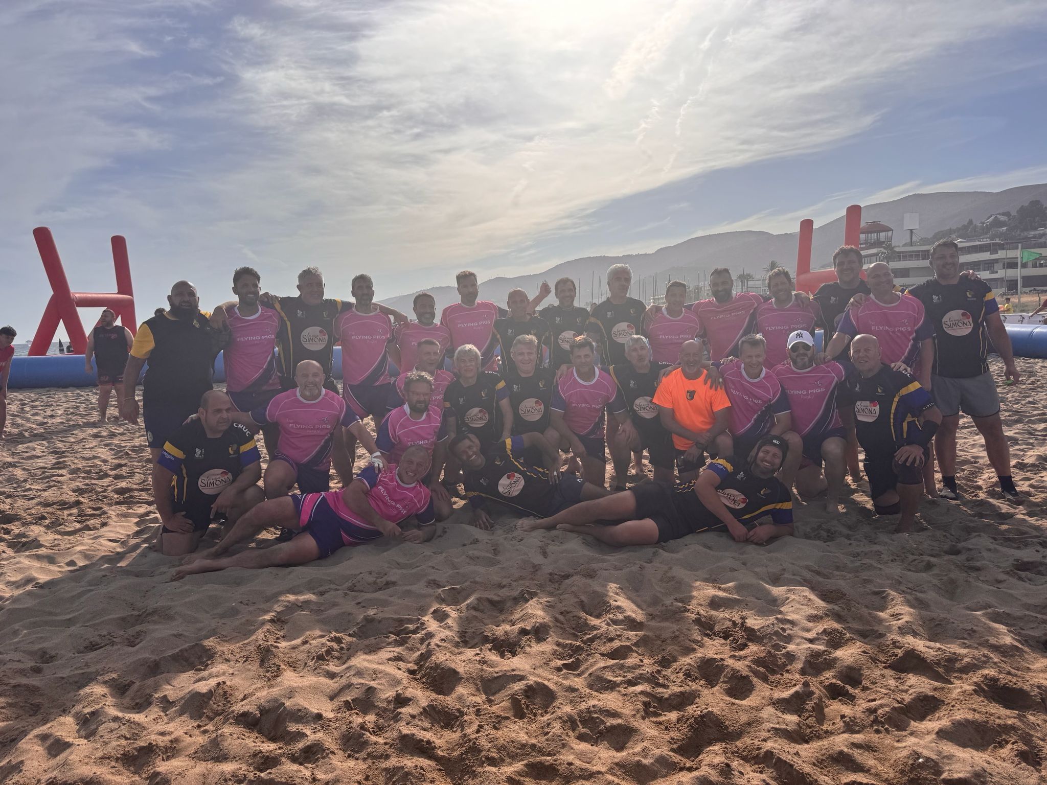 Foto de grup amb un equip rival a la sorra, amb el Garraf al fons